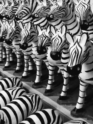 A collection of handmade zebra figurines arranged in rows on a wooden shelf, monochrome shot.